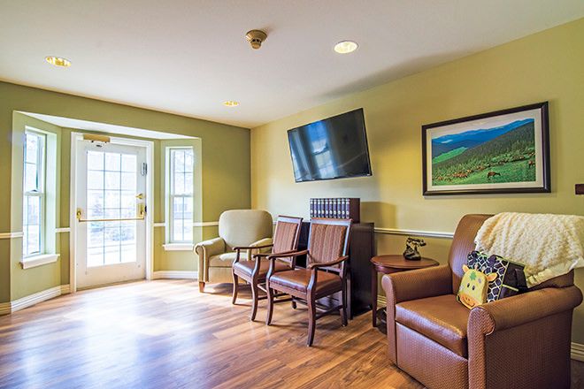 A cozy living room with various chairs, a mounted television, and artwork on the wall.