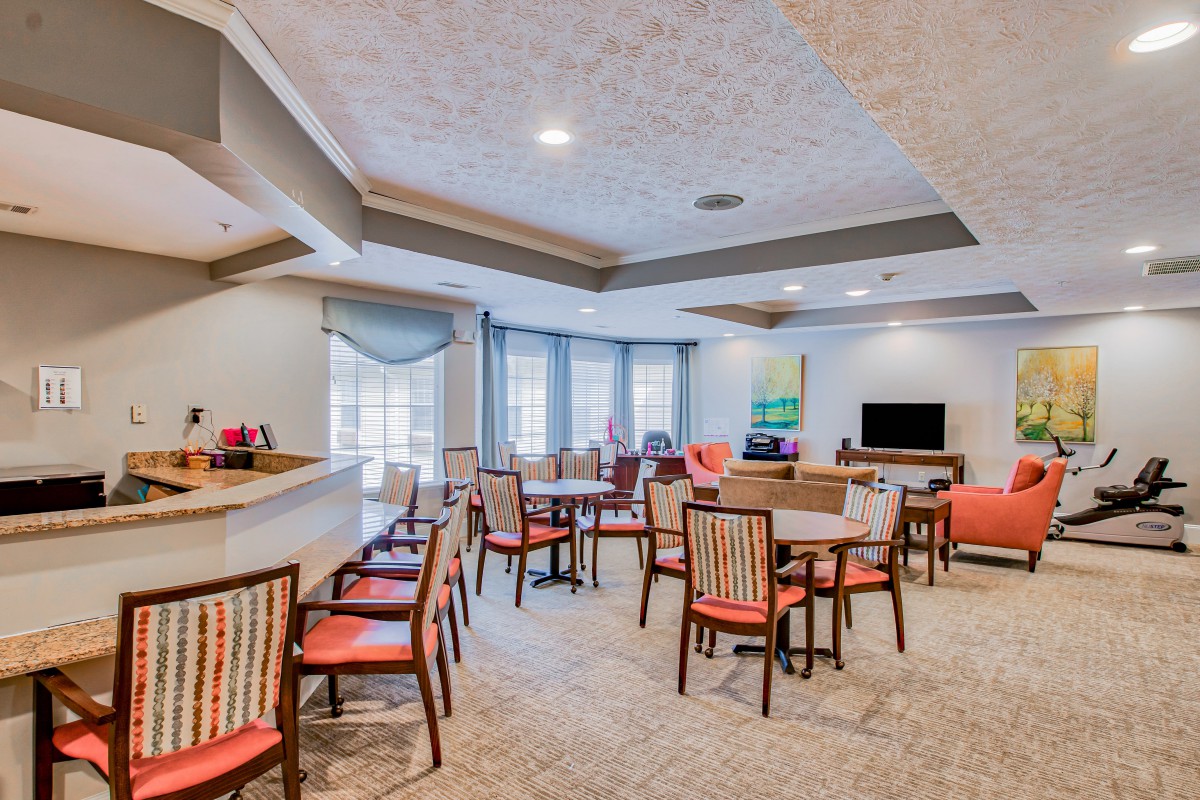 A modern dining area with seating and a television, featuring several tables and chairs.