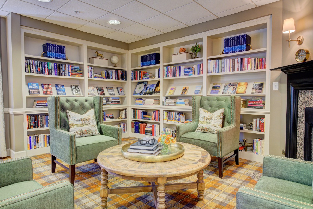 A cozy library setting featuring comfortable chairs and a round table surrounded by bookshelves.