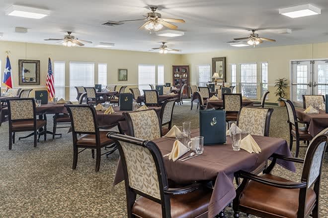 A well-arranged dining room with tables set for service, featuring ceiling fans and elegant decor.