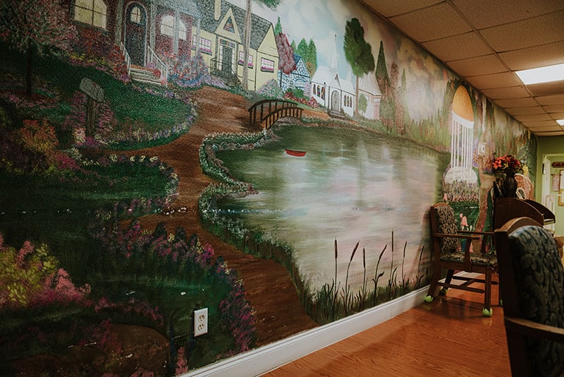 A detailed mural depicting a scenic landscape with houses, a lake, and a winding pathway.