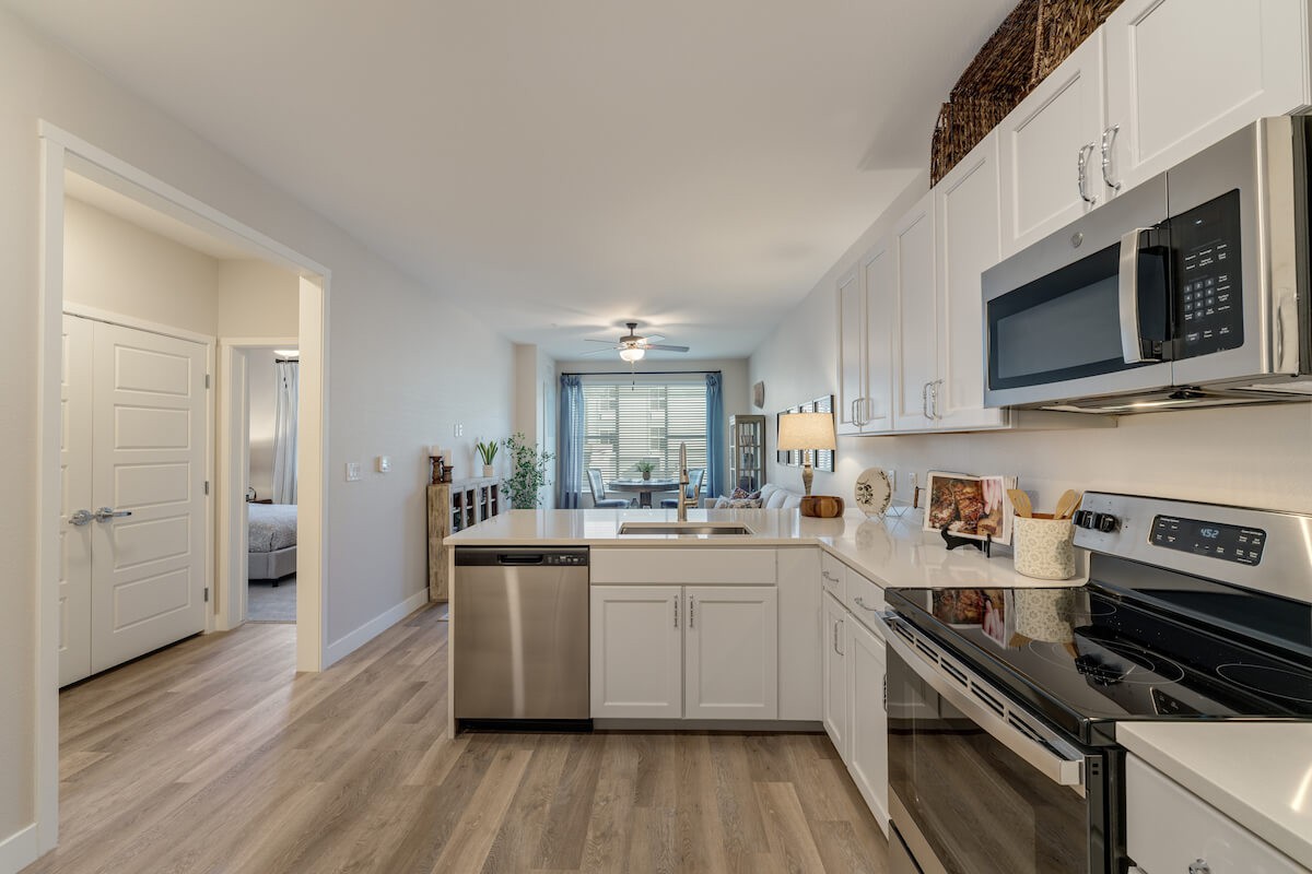 A modern kitchen with white cabinets and stainless steel appliances, featuring an open layout and hardwood flooring.