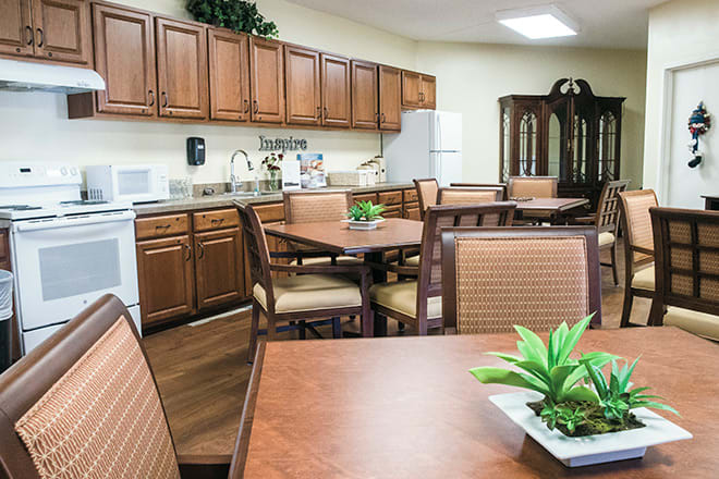 A cozy kitchen and dining area with wooden cabinets, tables, and chairs accented by indoor plants.