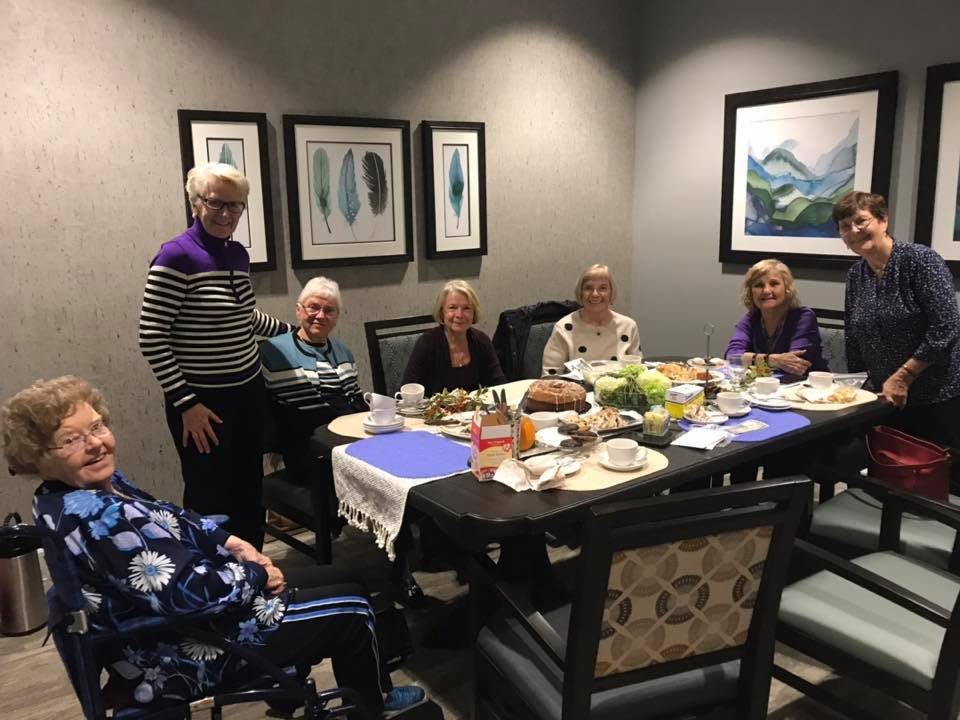 A group of seniors enjoying a meal together at a dining table indoors, surrounded by artwork on the walls.