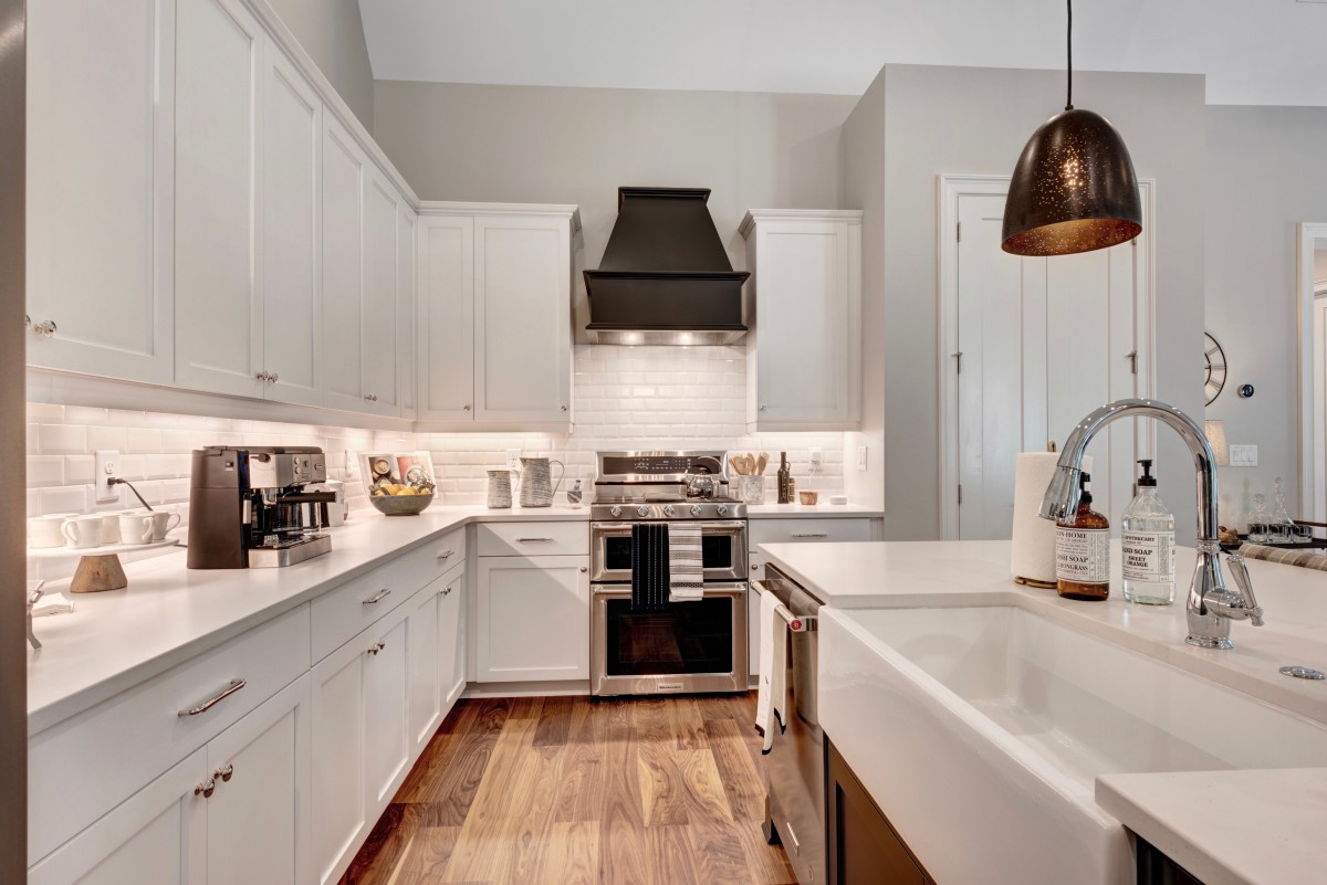 A modern kitchen with white cabinets, stainless steel appliances, and wooden flooring.