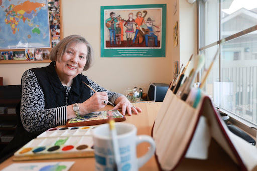 An artist happily engaged in painting at her studio, surrounded by tools and inspiration.