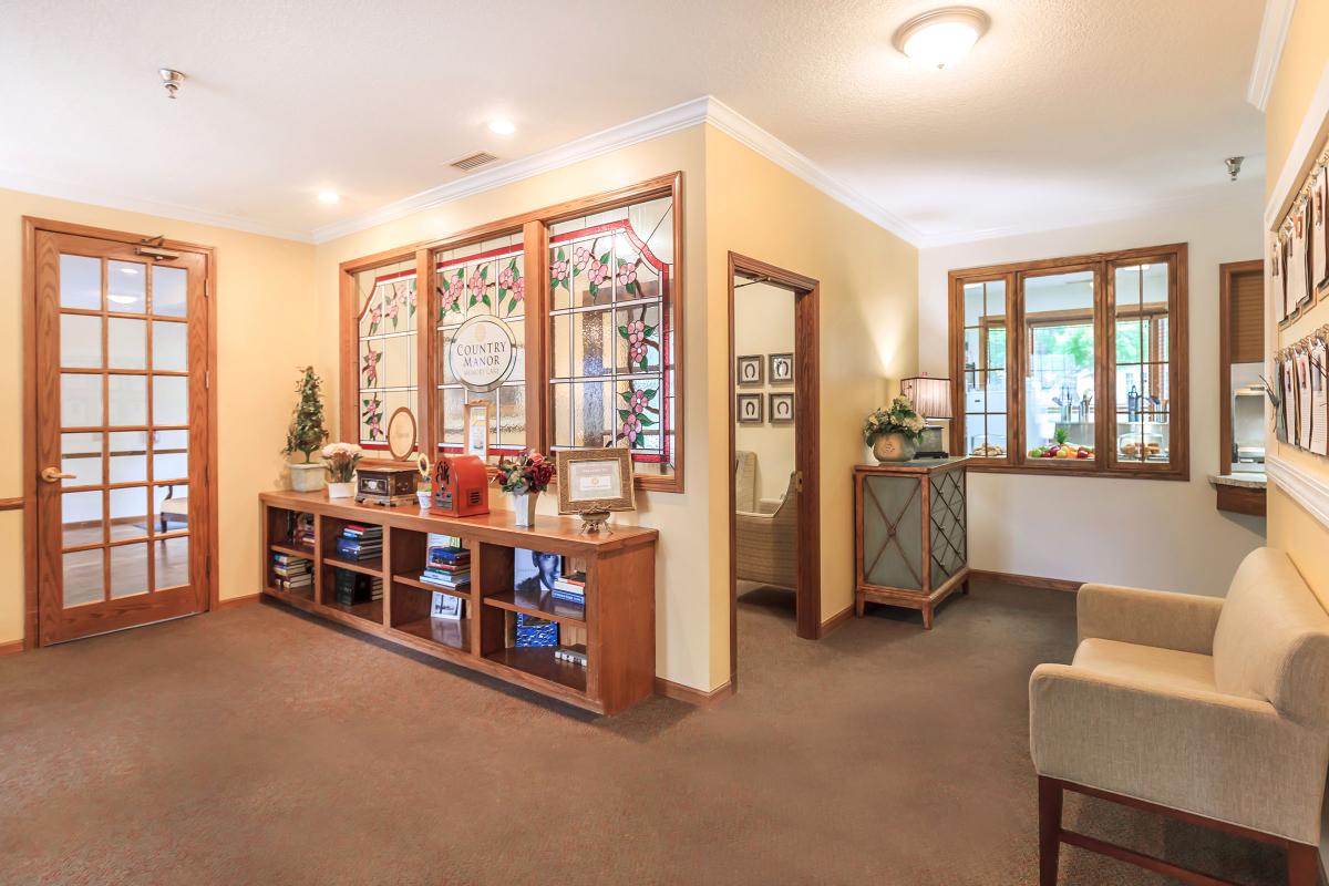 A cozy living room interior featuring a stained glass wall, carpeted floor, and wooden shelving with decorative items.