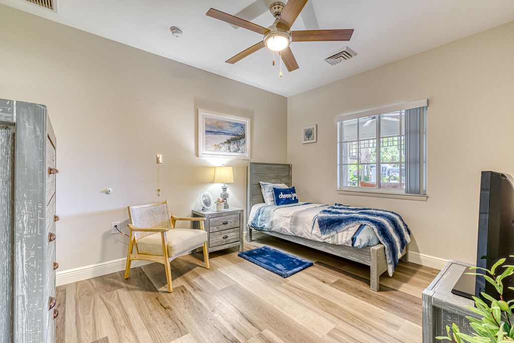 A cozy, minimalist bedroom featuring a single bed, wooden flooring, and a ceiling fan.