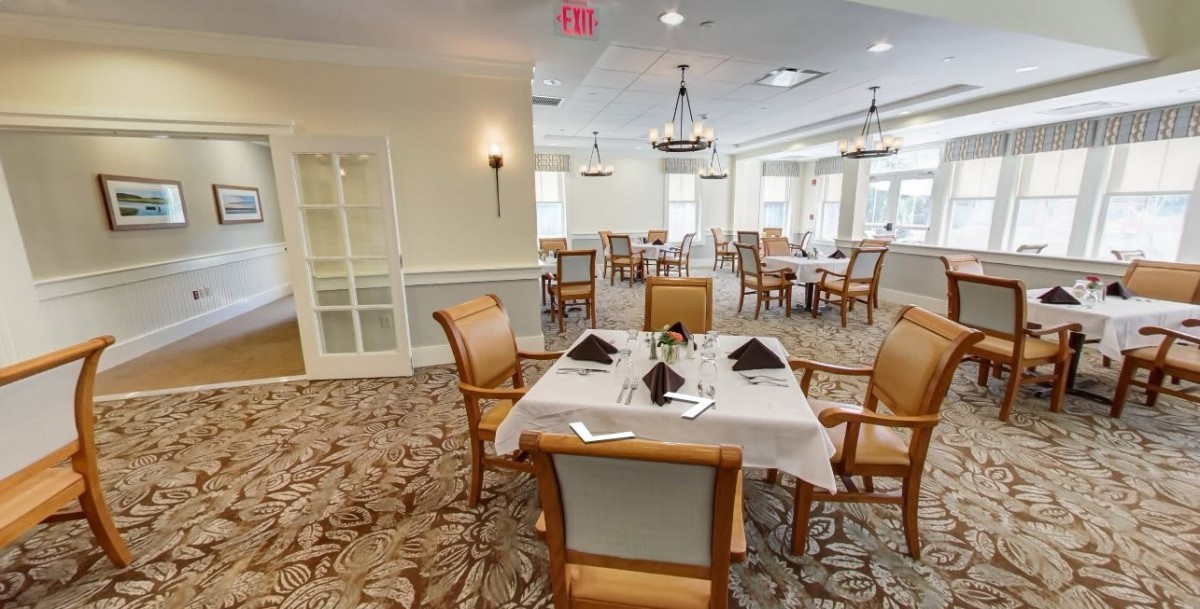 An elegant dining room with neatly arranged tables and chairs, featuring chandeliers and a carpeted floor.