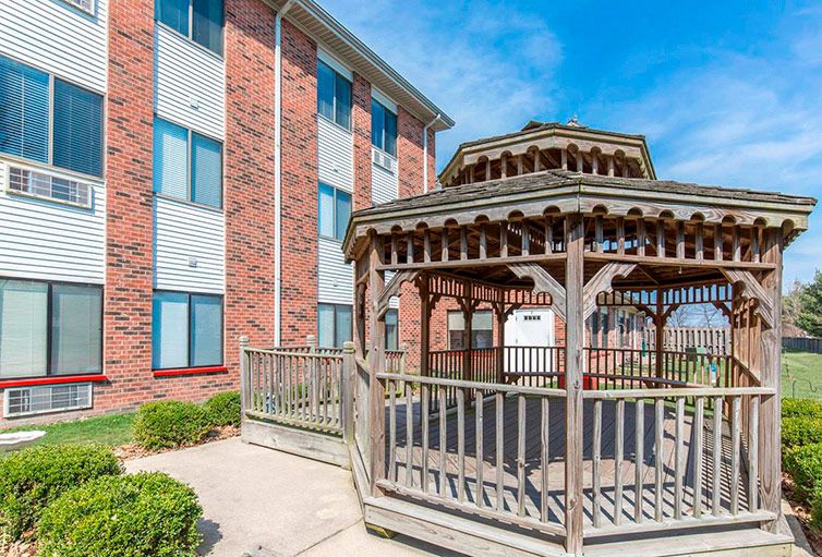 A sunny day view of a wooden gazebo next to a brick building.