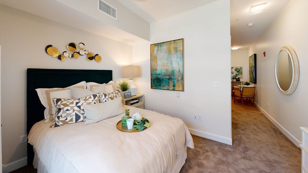 A modern and cozy bedroom featuring stylish decor with artwork on the wall and a neatly arranged bed.