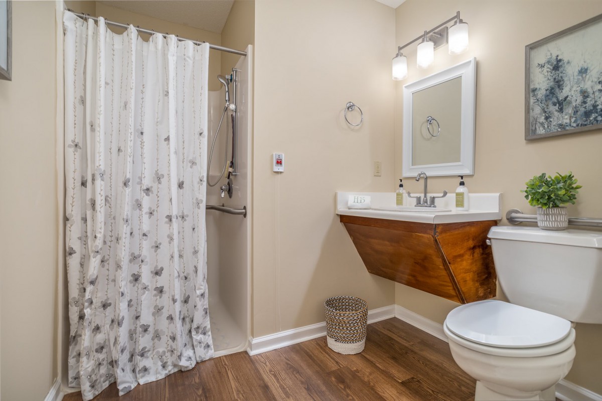 A modern bathroom with a wooden floor, featuring a sleek sink, shower curtain, and contemporary light fixture.