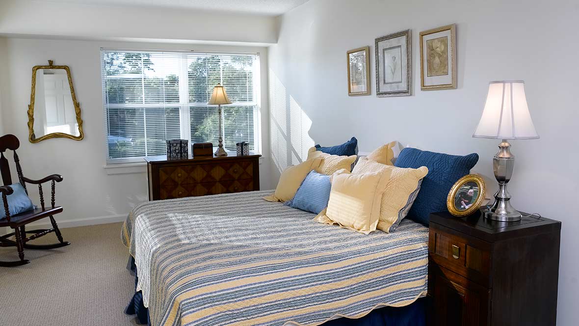 A cozy bedroom with sunlight streaming through a window, featuring a neatly arranged bed with striped bedding and decorative pillows.