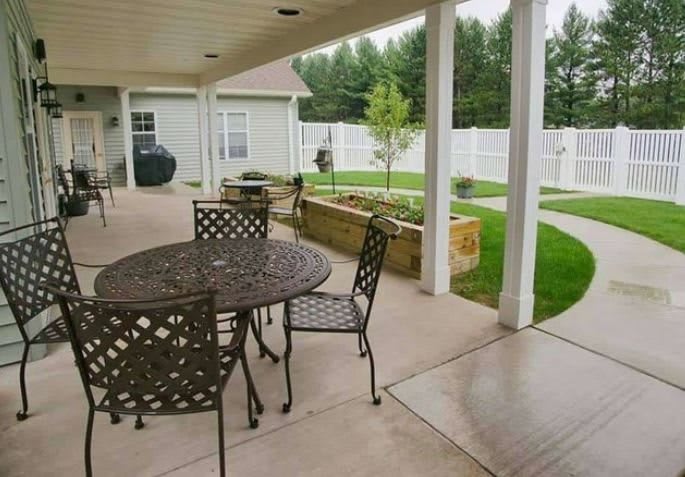 A covered patio with outdoor furniture overlooking a garden and fenced backyard.