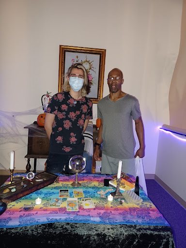 Two individuals standing in a mystical setting with a decorated table.