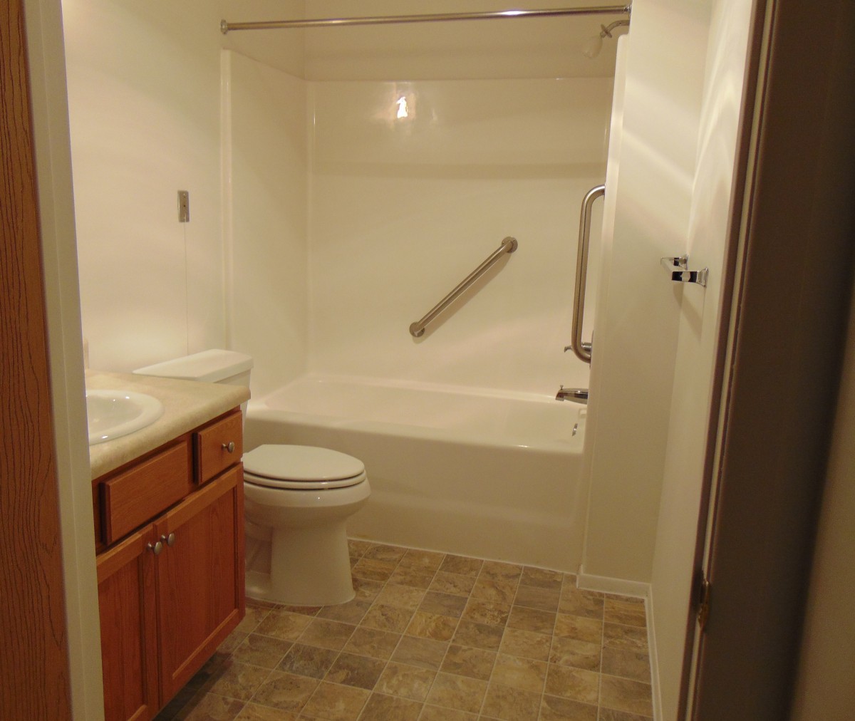 A small bathroom with a bathtub, toilet, sink, and grab bar.