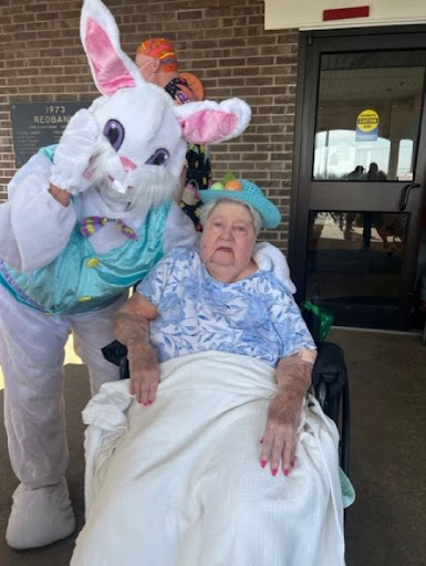 A joyful moment during an Easter celebration, featuring a person in a bunny costume with an elderly woman in a wheelchair.