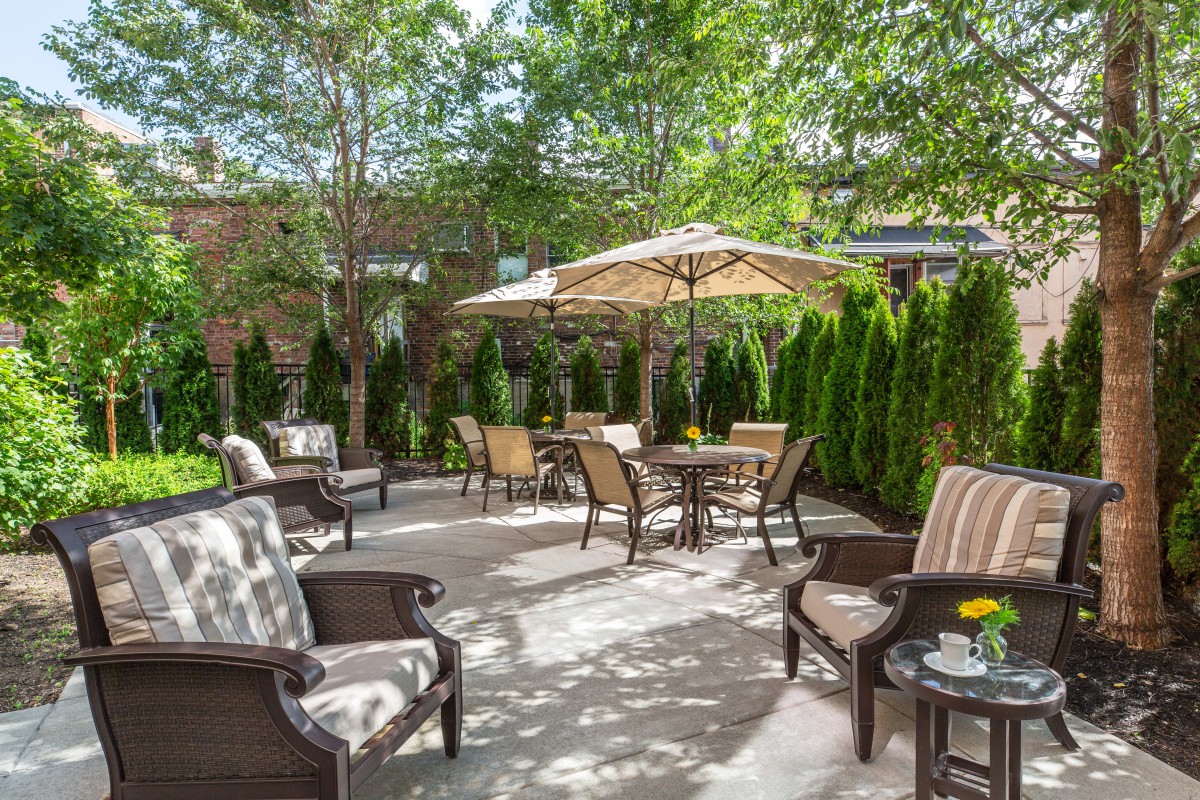 A cozy outdoor patio with chairs, tables, and umbrellas surrounded by lush greenery.