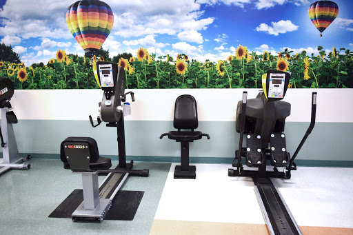 A fitness area featuring various workout machines against a vibrant backdrop of sunflowers and a hot air balloon.