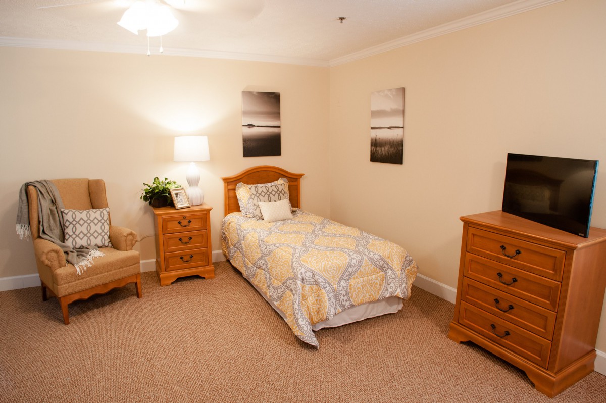 A cozy bedroom featuring a single bed, wooden furniture, and soft lighting complemented by wall art.