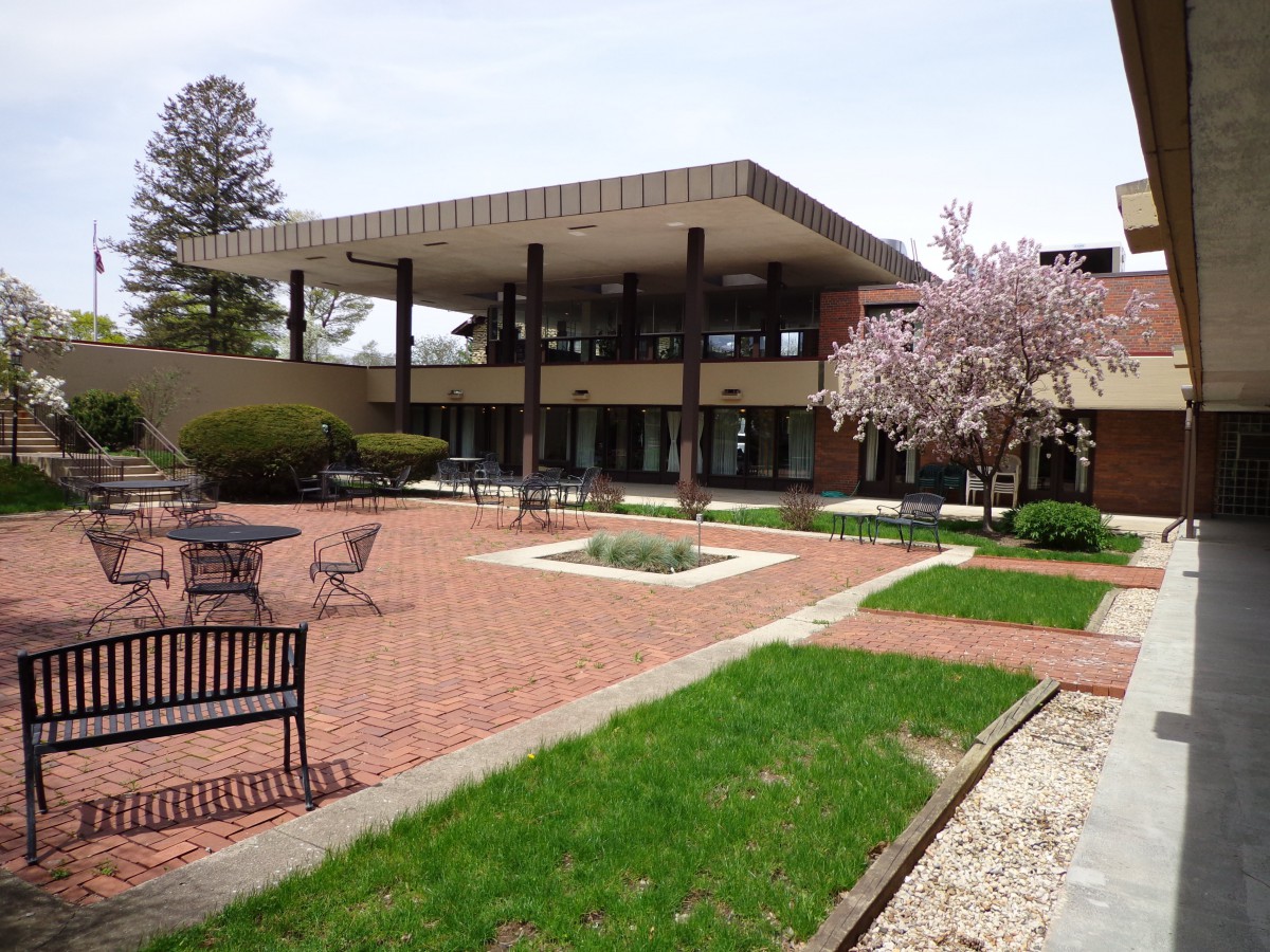 A modern building with a spacious courtyard featuring outdoor seating and blossoming trees.