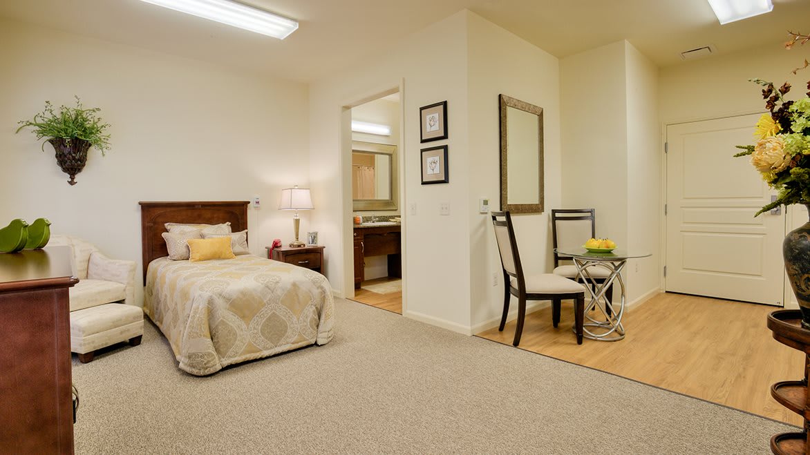 A cozy bedroom with a neatly made bed, a desk area with a chair, and a large mirror.