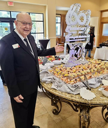 A formal event featuring an impressive dessert table, with a man in a suit proudly showcasing the spread.