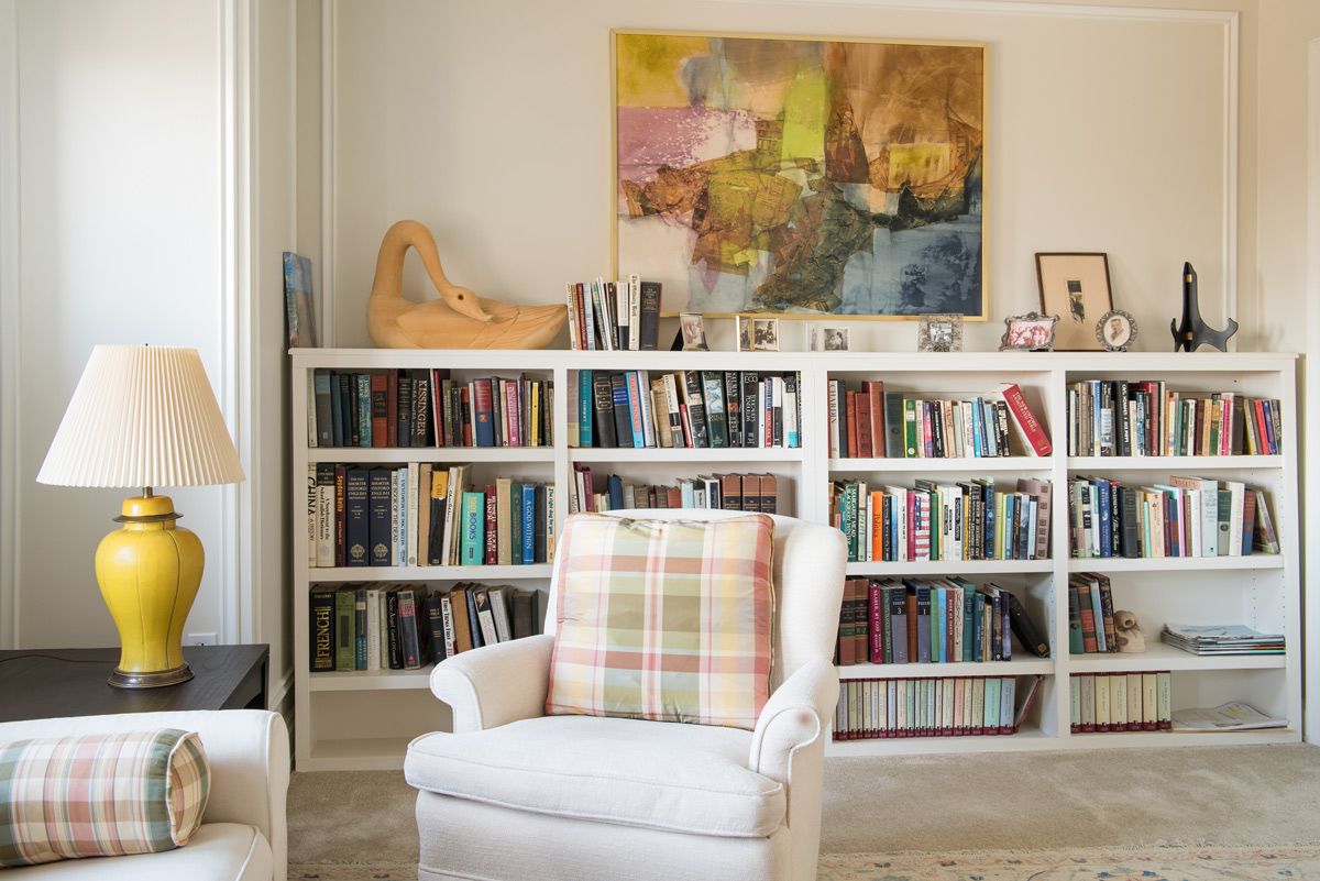 A cozy living room featuring a well-stocked bookshelf, a comfortable armchair with a plaid pillow, and abstract artwork on the wall.
