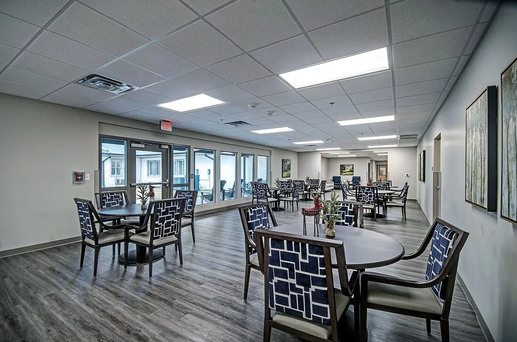 A modern dining area with neatly arranged tables and chairs, illuminated by bright ceiling lights.