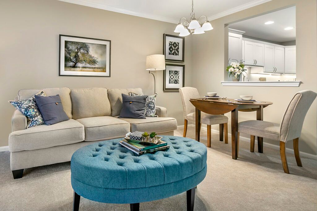 A cozy living room with a beige sofa, blue tufted coffee table, and a dining area in the background.