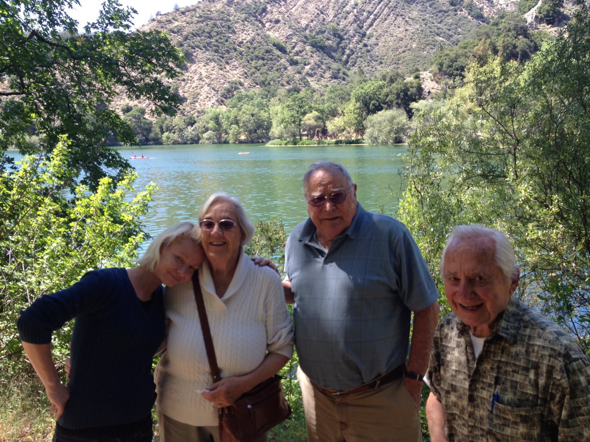 A group of people posing together in front of a lake with trees and hills in the background.