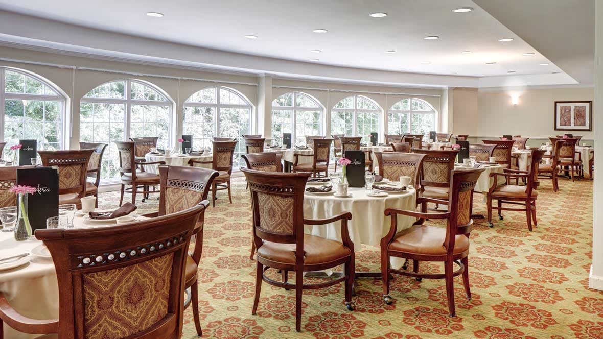 Elegant dining area with neatly arranged tables and chairs, featuring large windows providing natural light.