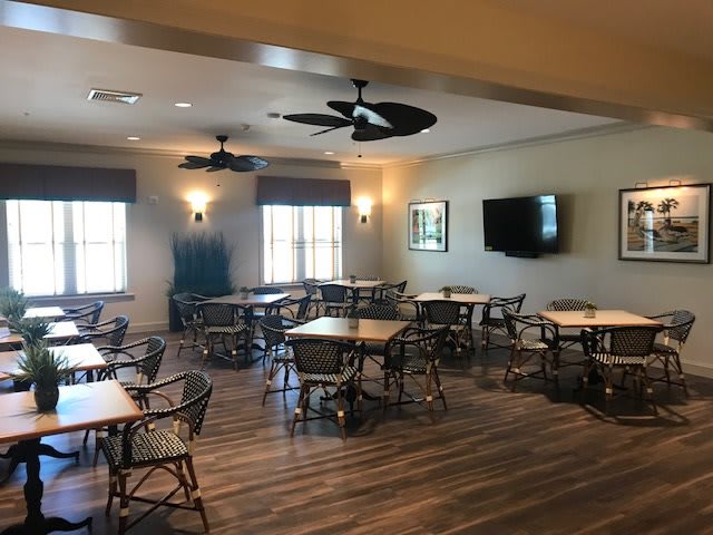 A dining area with multiple tables and chairs, featuring ceiling fans and a television.