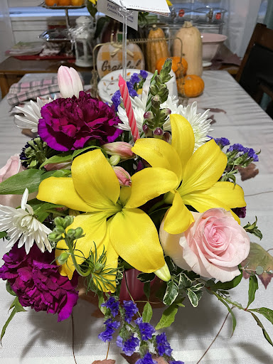 A vibrant bouquet featuring yellow lilies, pink roses, and rich purple carnations.
