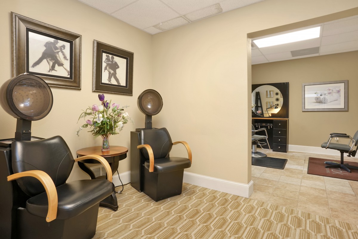 A salon waiting area featuring comfortable chairs, a hairdryer, and decorative artwork.