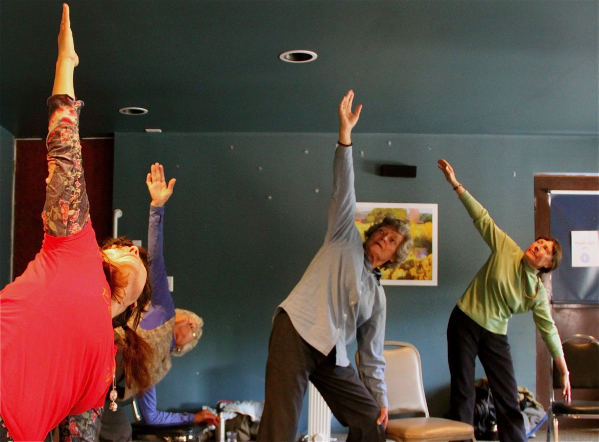 A group of people practicing yoga indoors, performing a stretching exercise together.