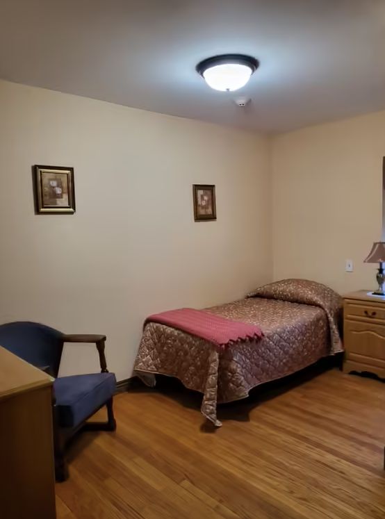 A simple bedroom with a single bed, dresser, and chair.