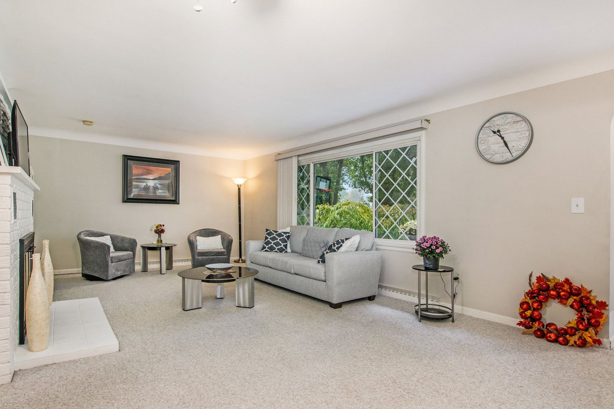 A cozy living room with a sofa, chairs, and a large window overlooking greenery.