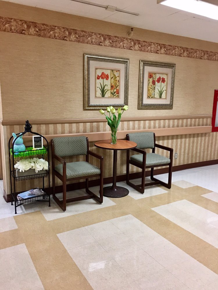 A cozy waiting area with two chairs, a small table with a vase of flowers, and framed artwork on the wall.