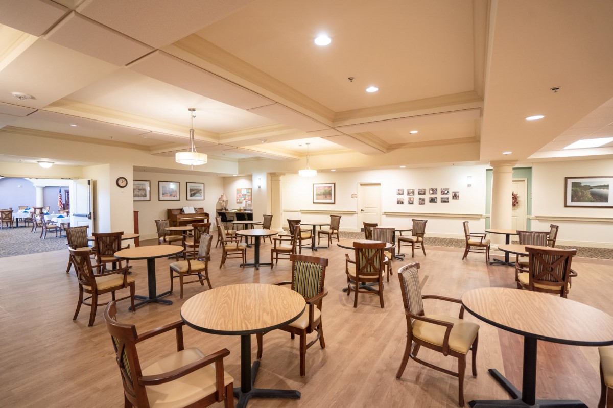 An empty dining room with wooden tables and chairs, featuring warm lighting and decorative wall art.