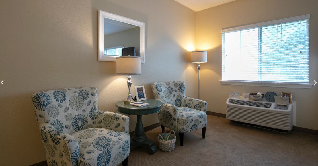 A cozy living room corner with two patterned armchairs and a small round table, complemented by a standing lamp and wall mirror.