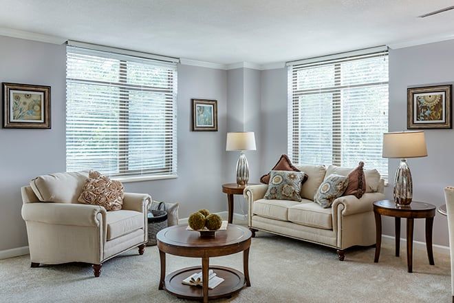A cozy living room with a sofa, armchair, and coffee table, illuminated by natural light from large windows.