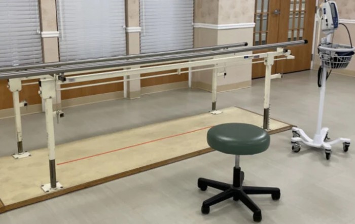 A physical therapy room featuring parallel bars and a stool for rehabilitation exercises.