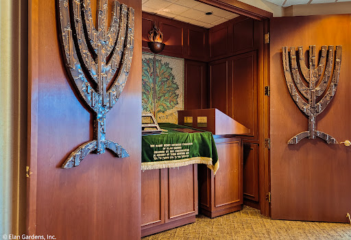 A view of the interior of a synagogue featuring wooden menorah decorations and a green Torah cover.