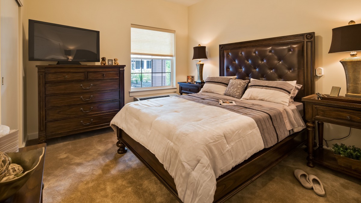 A cozy bedroom featuring a large bed with a tufted headboard, a dresser, and a bedside lamp.