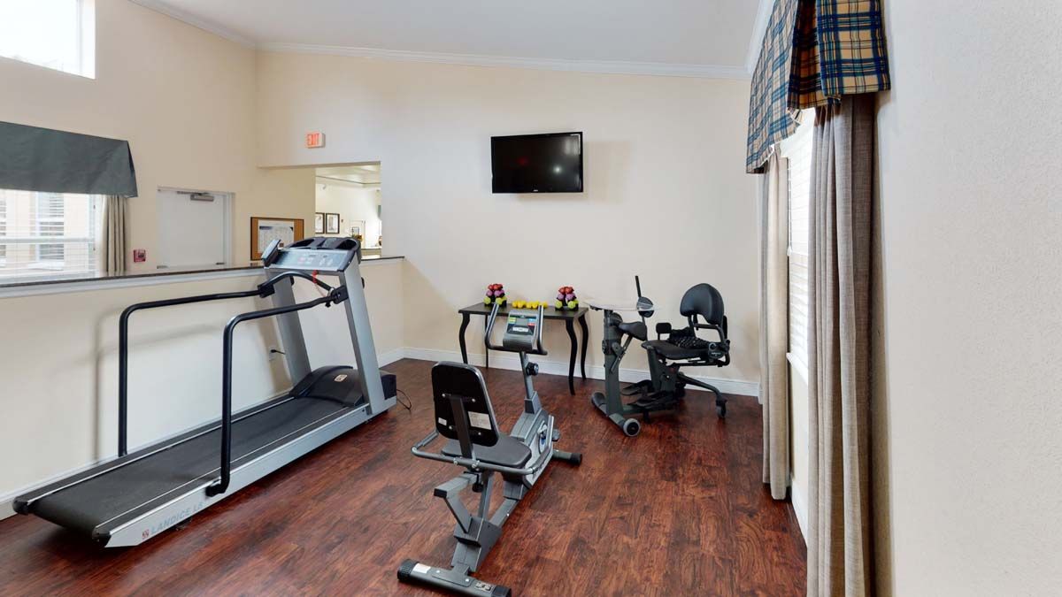 A small gym with fitness equipment, including a treadmill and exercise bike, with a TV mounted on the wall.