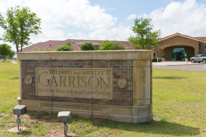 Entrance sign for the building named 'Garrison' with a brick structure and greenery.