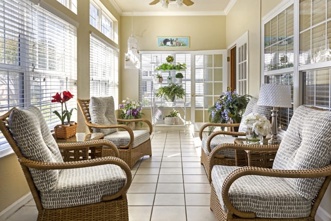 A cozy sunroom featuring rattan furniture and indoor plants, filled with natural light.