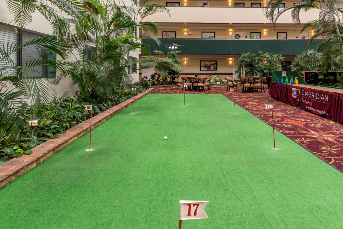 An indoor mini-golf course in a hotel lobby with lush plants and an artificial turf green.