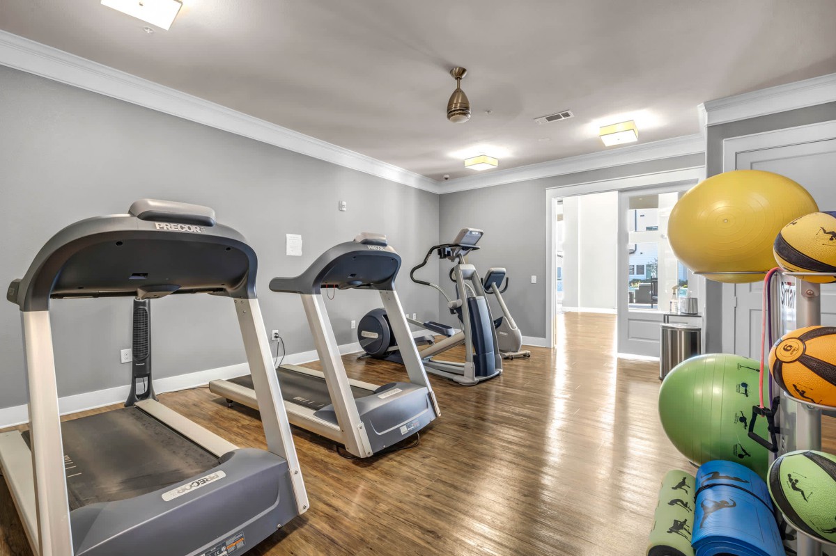 A modern gym with treadmills and exercise equipment on a wooden floor.